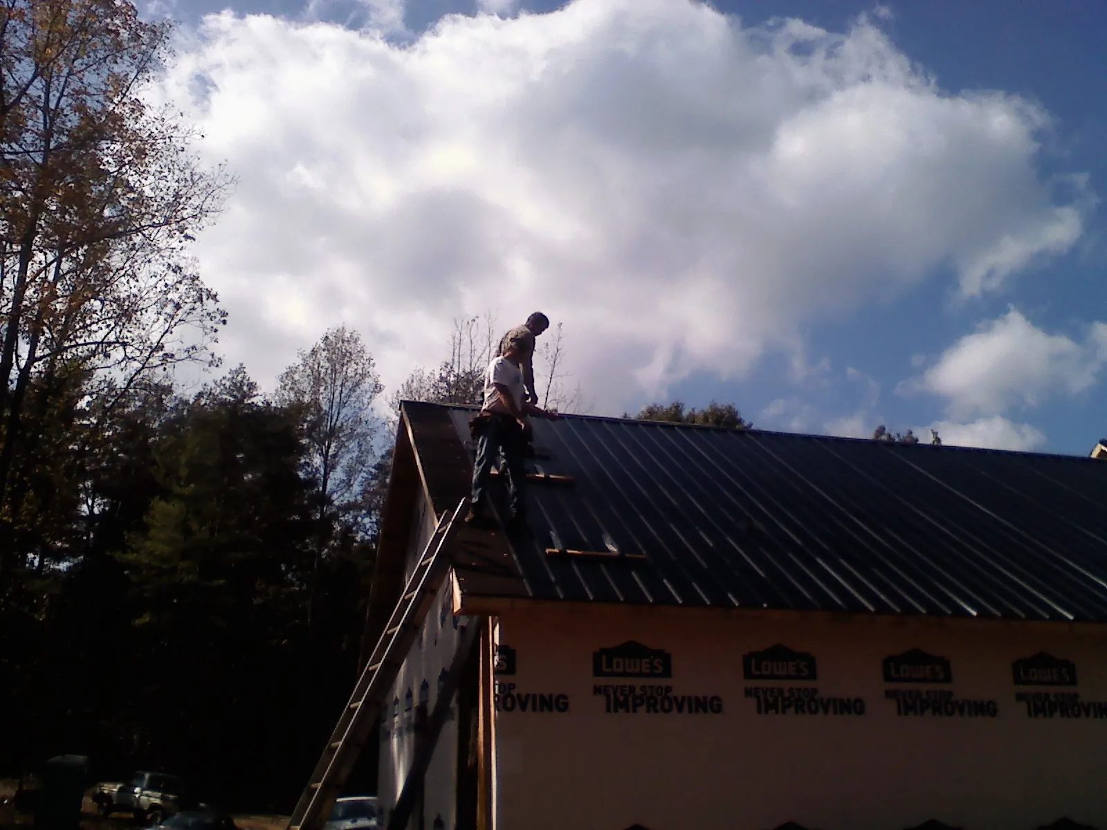 Roofer fastening dark metal panels high against a cloudy sky, from a Roof Inspection job in Saint Helena