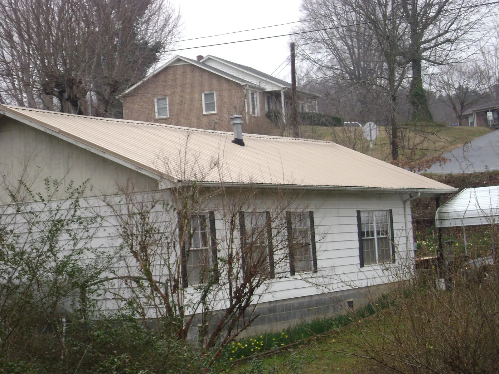 Tan metal roof on a white sided house set into a hillside — Commercial Roofing by Roofing Brothers in Saint Helena